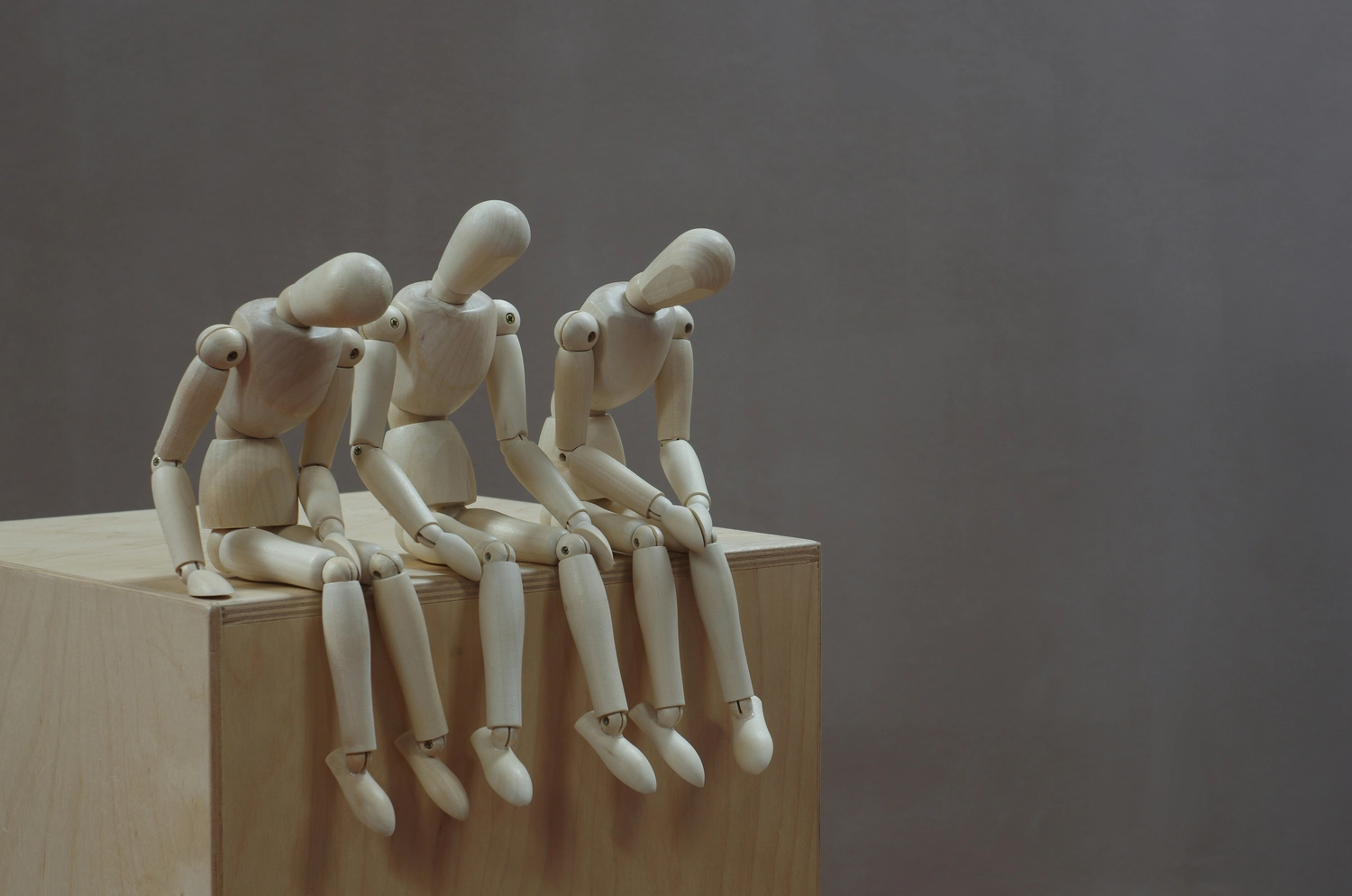 Drei Holzfiguren seitzen auf einer Holzkiste. Alle drei schauen müde und ausgelaugt nach unten, denn sie leiden an ME/CFS