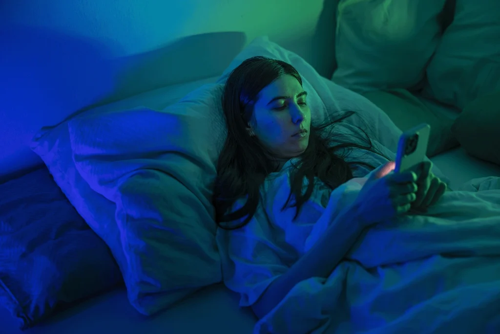 Eine Frau liegt im Bett und liest etwas auf ihrem Mobiltelefon. Sie leidet an ME/CFS und darum geht es in dem Blog von Constanze Ertl.