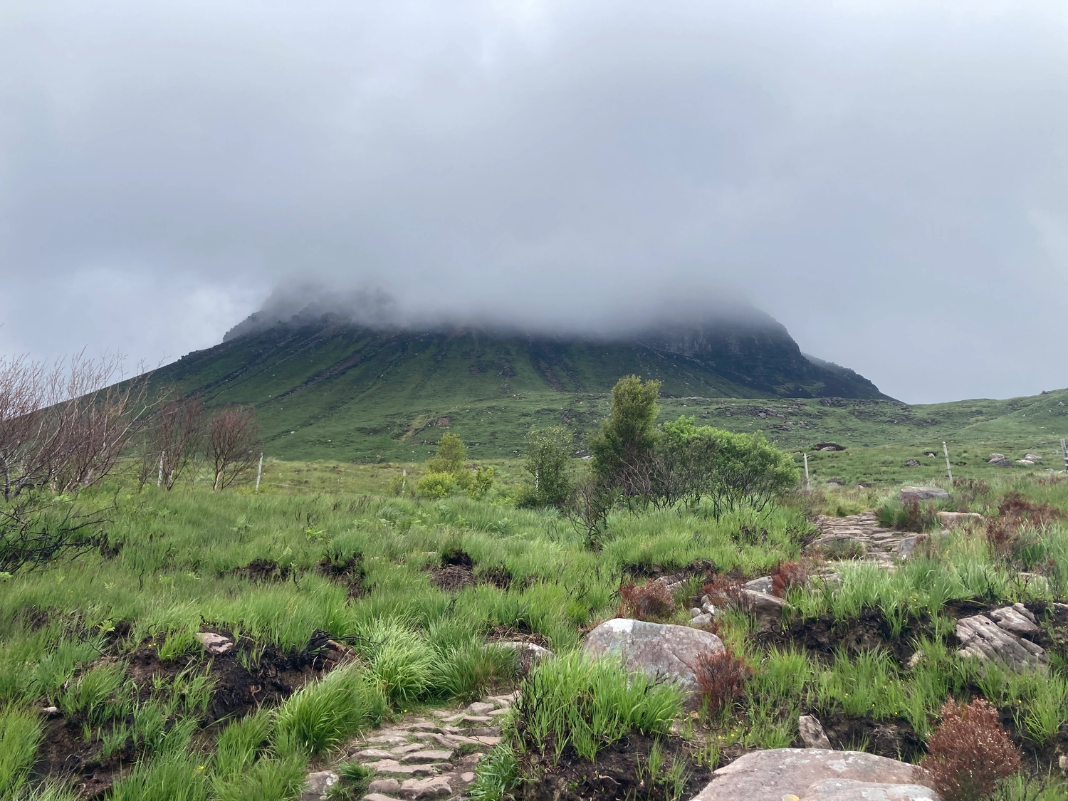 Ein Berg aus der Ferne, der Weg zum Gipfel ist erkennbar, aber der Gipfel ist im Nebel.